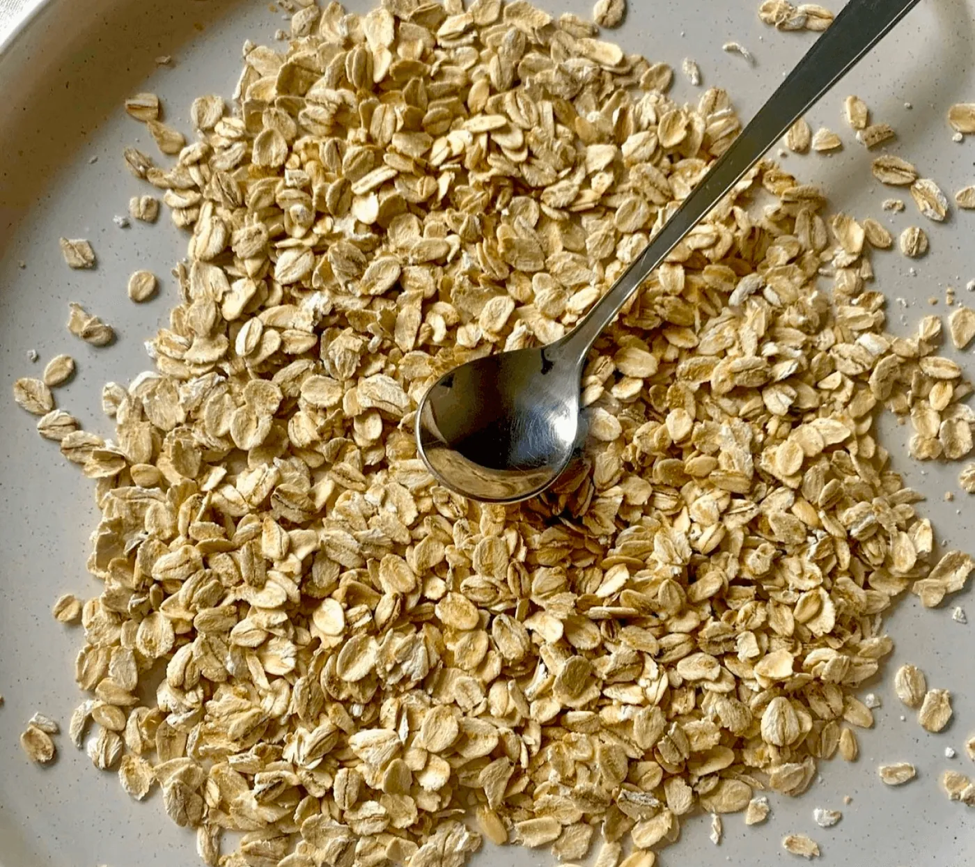 A pile of golden jumbo oats with a metal spoon