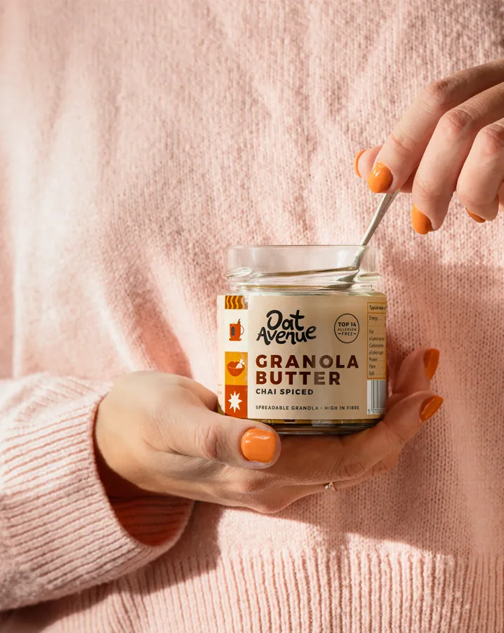 A hand holding an open jar of Chai Spiced granola butter with a spoon